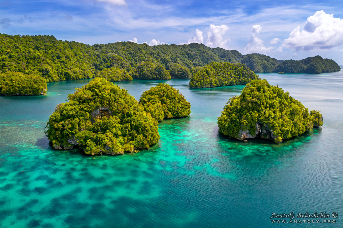 3 small mushroom shaped Rock islands in front of a big Rock island in Palau shot by a drone roughly 30 meters above ground by photo journalist Anatoly Beloschin